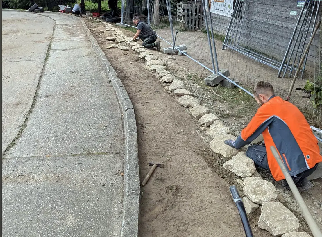 Helfer bauen eine Trockenmauer aus Naturstein entlang des Weges