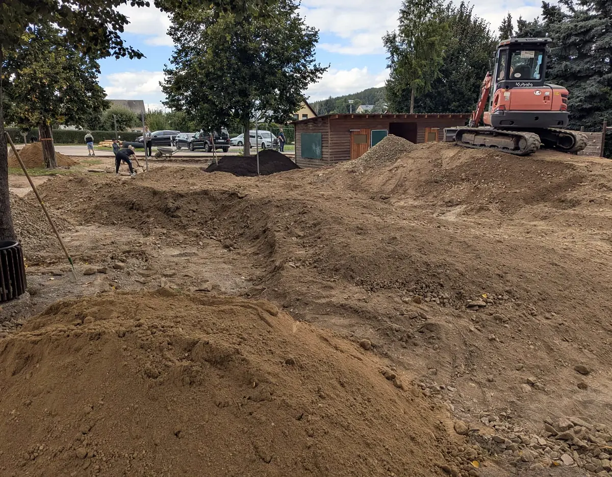 Der neue Schulhof der Grundschule Ruppendorf: modellierte Erdhügel und Bagger vor dem Schulgebäude